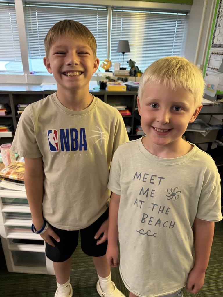 Two young boys smiling side-by-side, one in a beige NBA t-shirt and the other in a grey "Meet Me At The Beach" shirt.