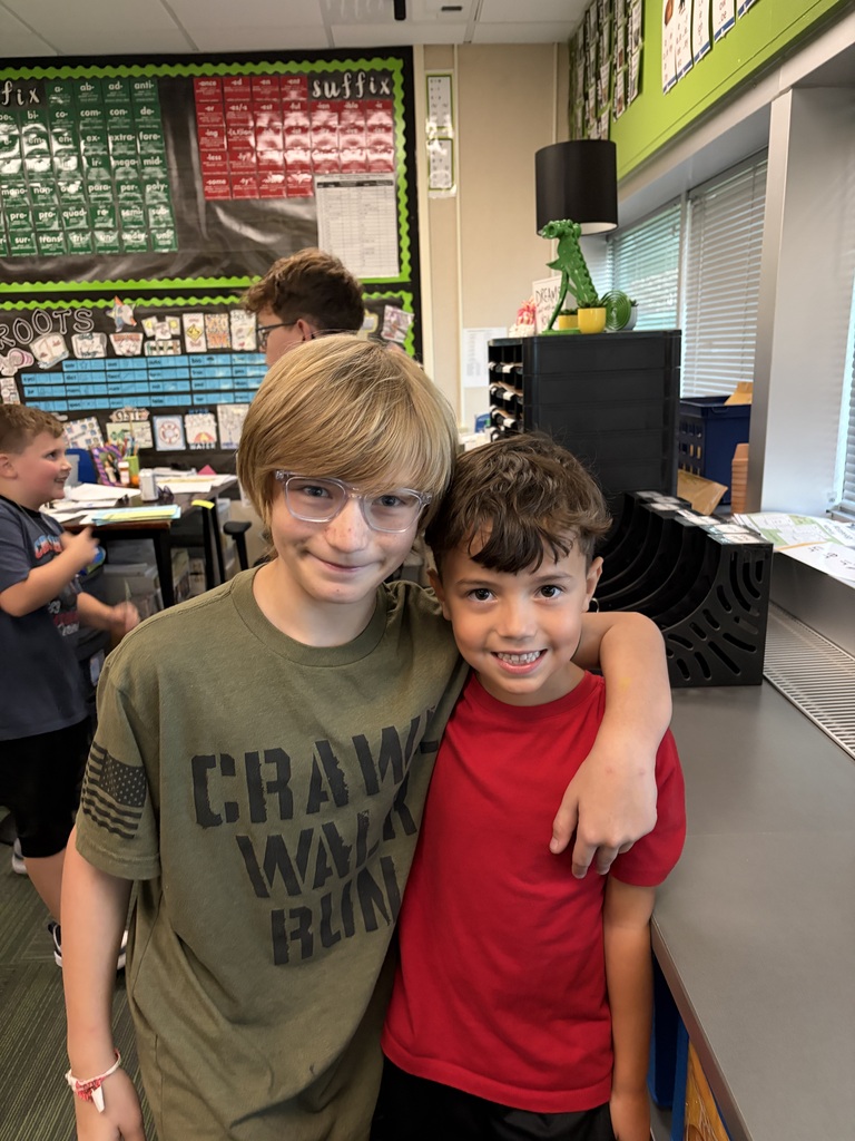 Two young boys with arms around each other, one in an olive green shirt and glasses, and the other in a red t-shirt.