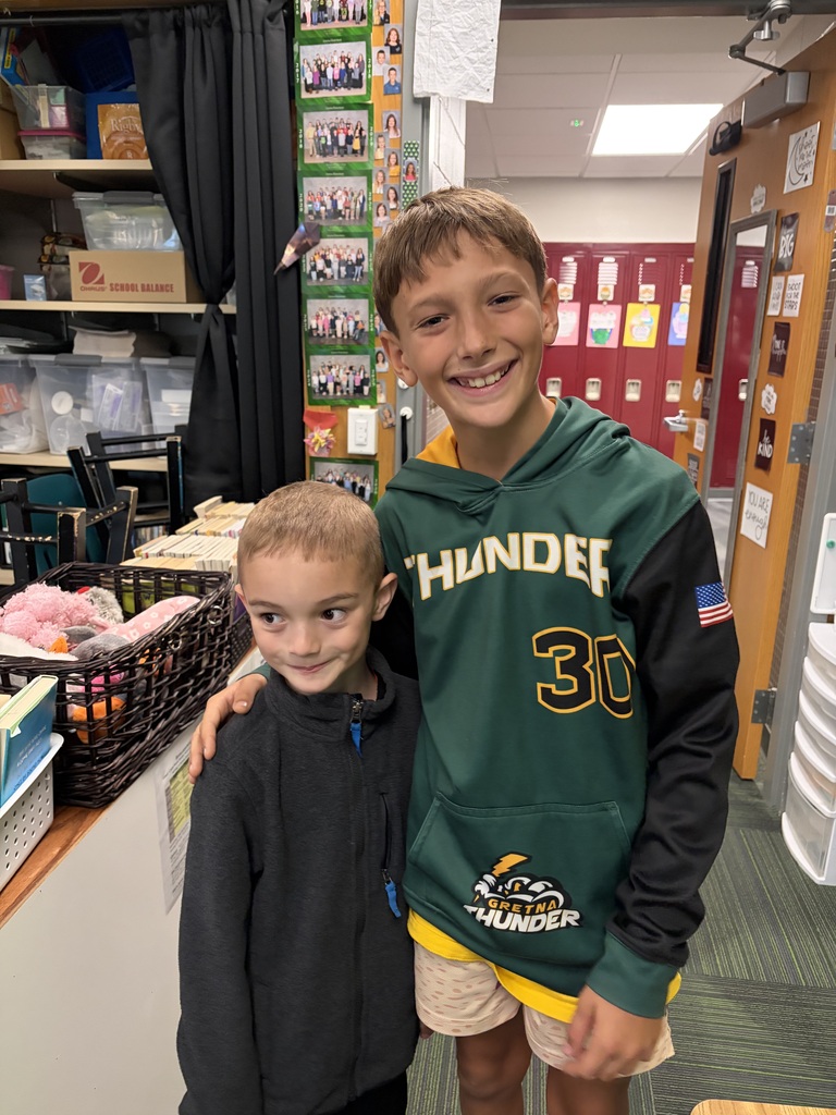 Two young boys posing in a doorway, the taller boy wearing a green Gretna Thunder hoodie with his arm around the smaller boy in a dark zip-up jacket.