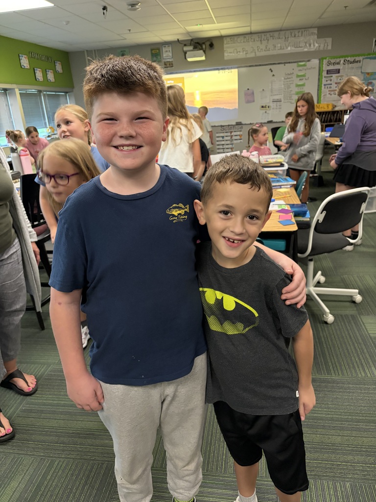 Two young boys standing together, one in a navy blue shirt and the other in a dark grey Batman shirt.