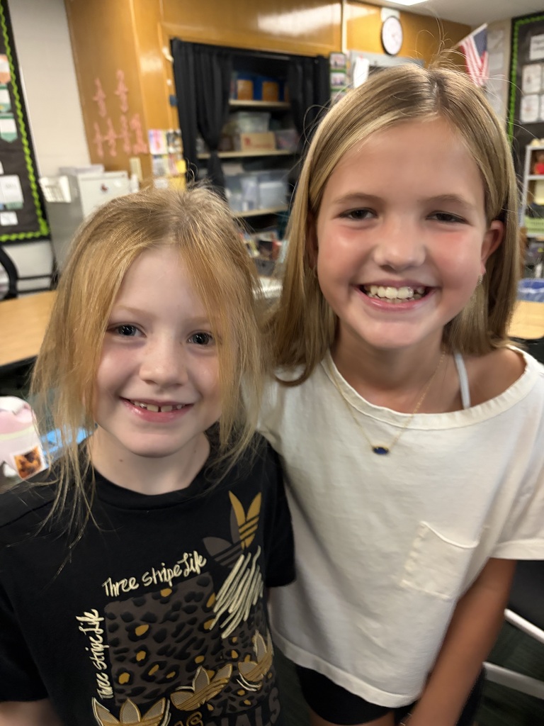 Two young girls smiling closely, one in a black "Three Stripe Life" shirt and the other in a white top with a pocket.