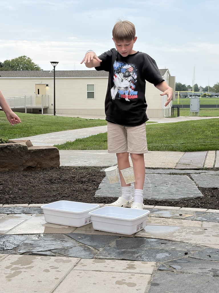 A boy dropping paper cups into plastic tubs of water during an outdoor science activity.