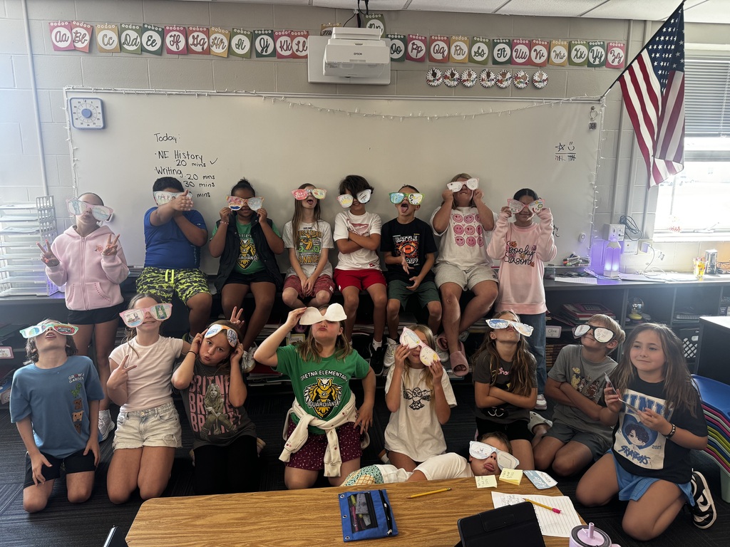 The full class of students posing playfully and smiling together while showing off their illustrated paper cutout sunglasses.