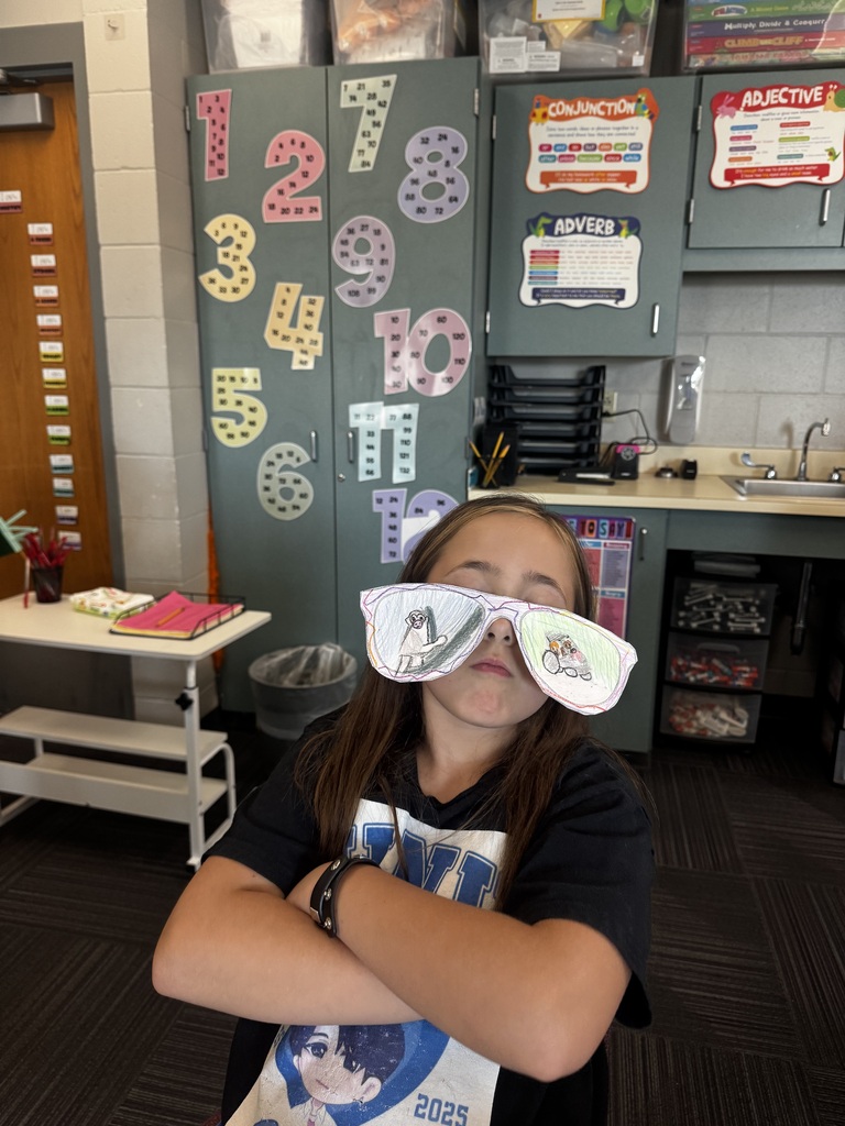 A student sitting with arms crossed, wearing oversized paper cut-out sunglasses featuring drawings of a light pole and a playground area.