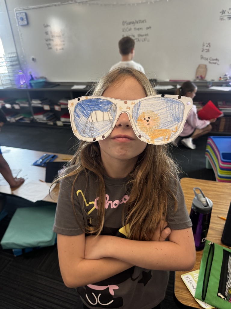 A girl with crossed arms wearing paper cutout sunglasses decorated with drawings of a tent and a friendly lion face.