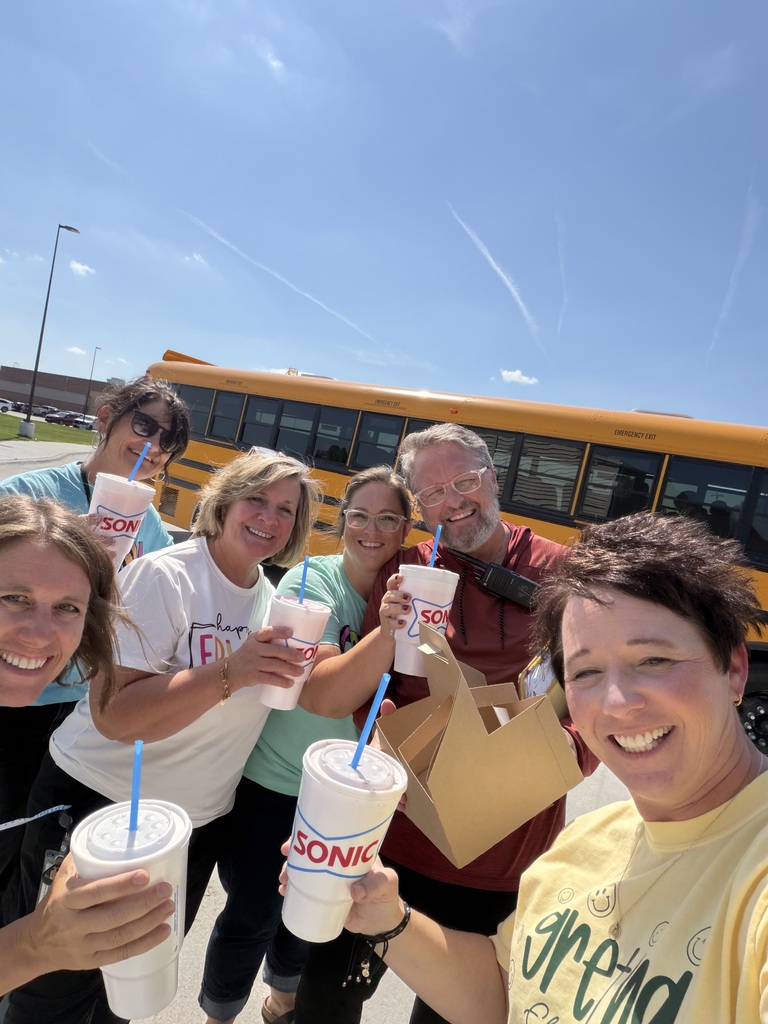 Group of teachers standing around a bus holding drinks and smiling