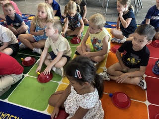 kidnergarteners on a rug in class with bowls learning about positions