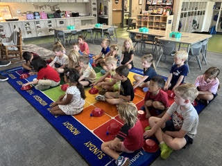 kidnergarteners on a rug in class with bowls learning about positions