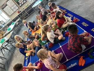 kidnergarteners on a rug in class with bowls learning about positions