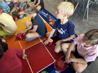 kidnergarteners on a rug in class with bowls learning about positions