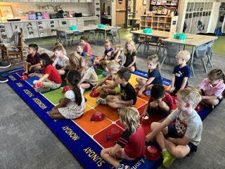 kidnergarteners on a rug in class with bowls learning about positions