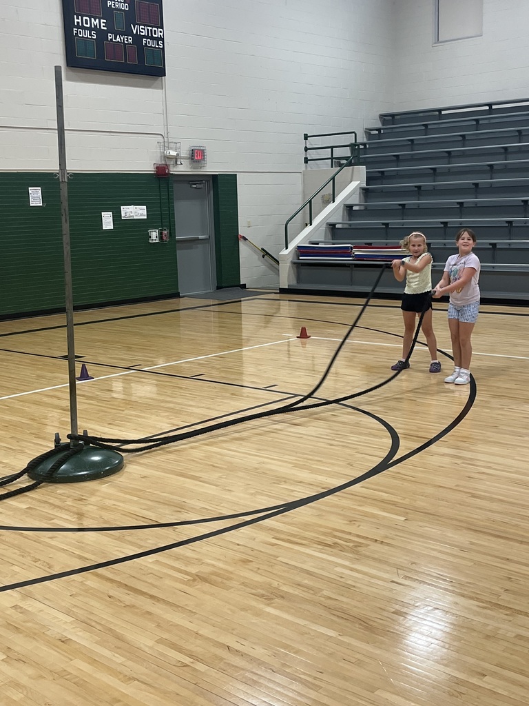 Two girls working together to wave a heavy battle rope attached to a pole in a gymnasium.