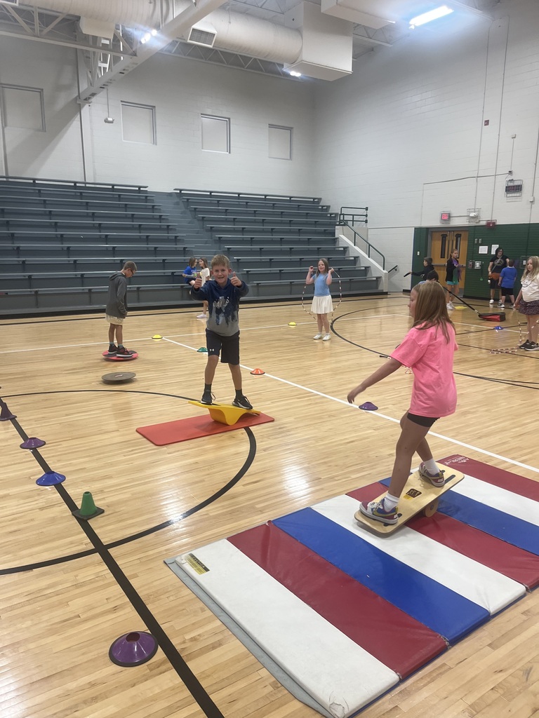 Students practicing balance training on balance boards and rocker boards placed on mats in a gymnasium.