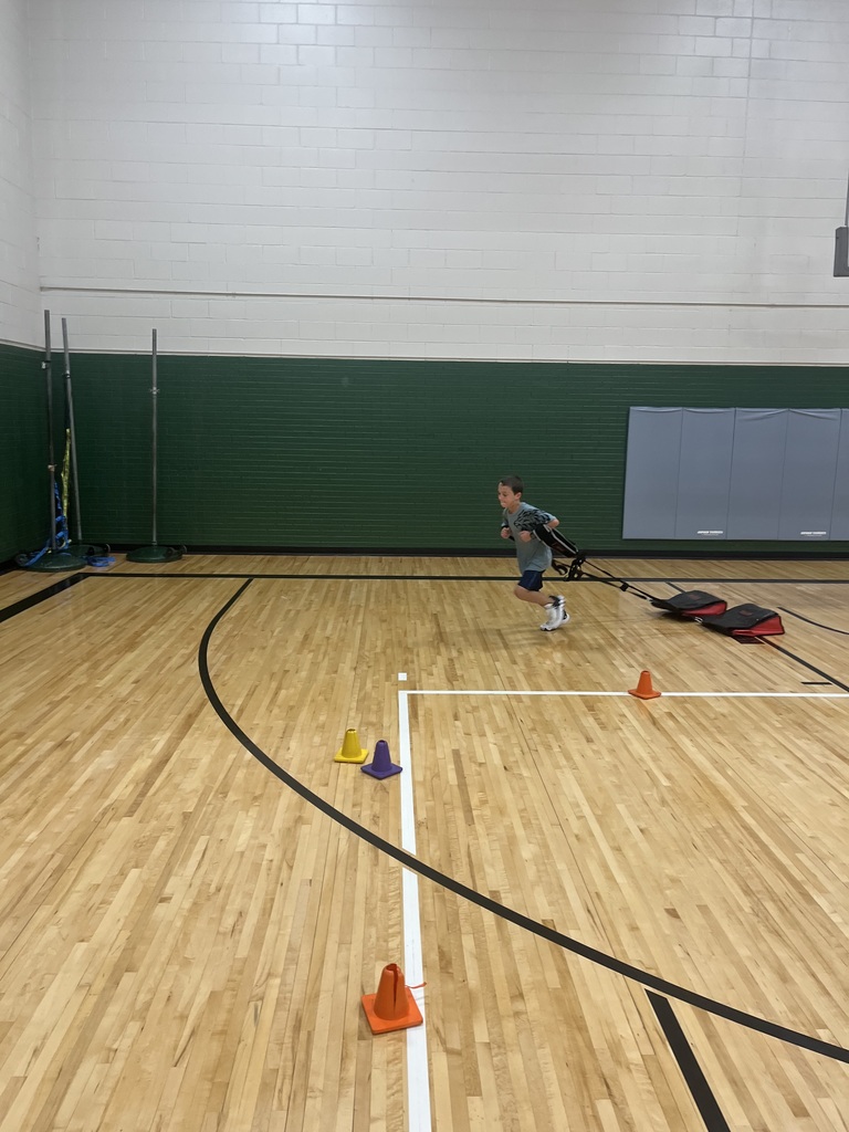 A boy running while pulling a weighted sled harness across a gymnasium floor.