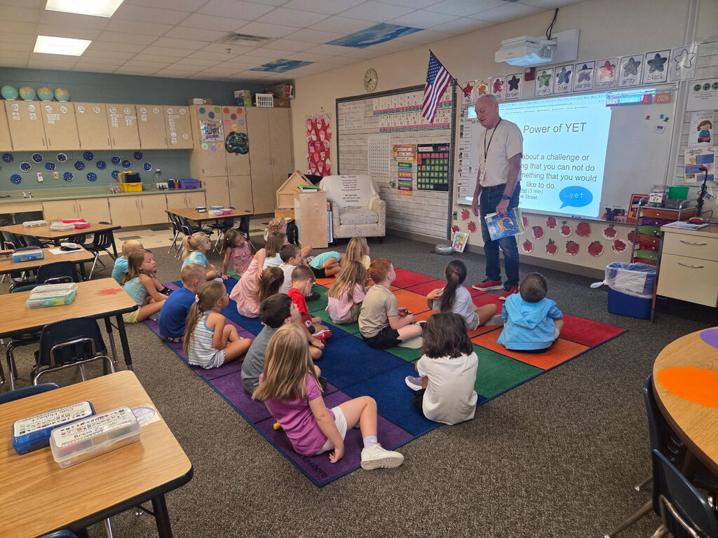 Kindergarten students are sitting on the rug learning "the power of YET" from Mr. Lenny, who is standing at the front of the room.