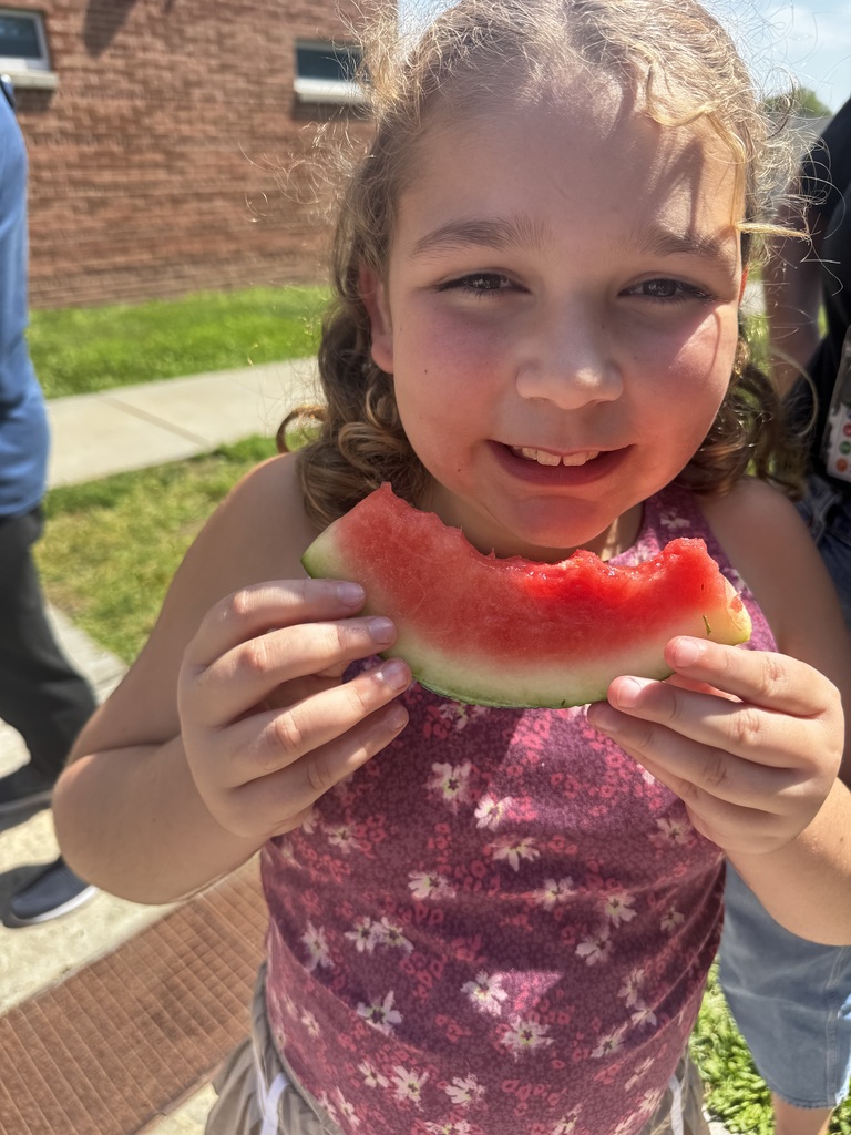 A close-up shot of a young girl smiling as she holds a partially eaten slice of watermelon in both hands.