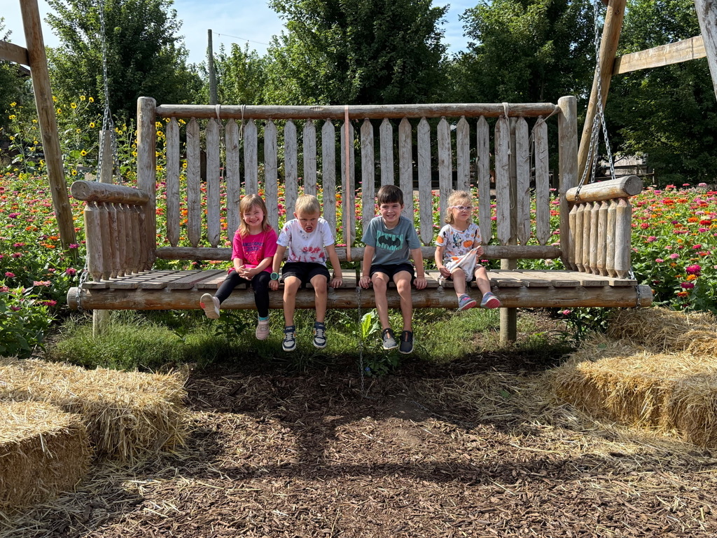 4 students are sitting on a giant, oversized bench swing