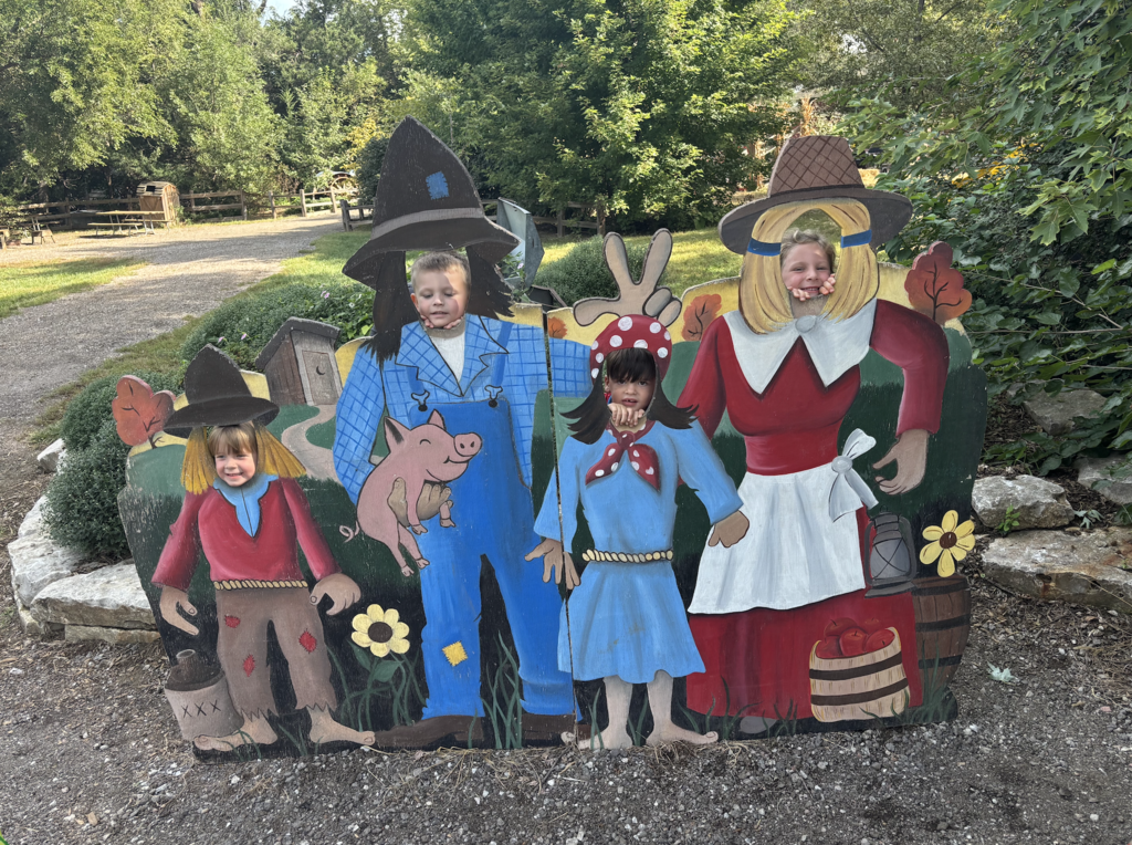 4 students' faces are through cut outs in a farm family body