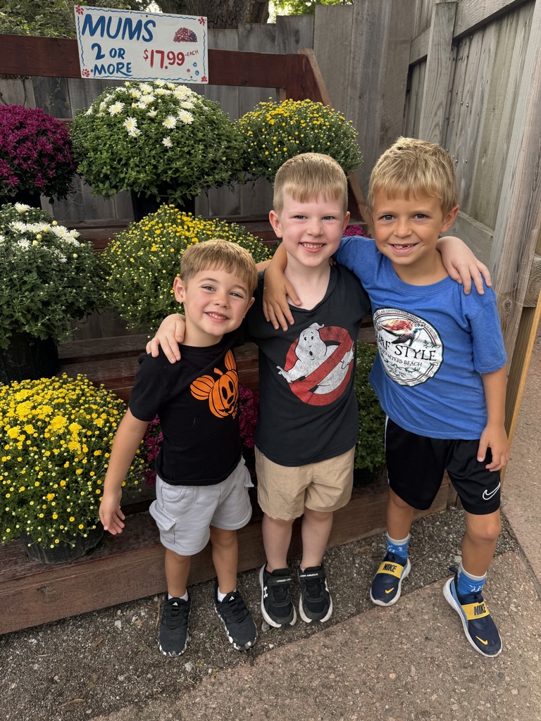3 students are standing in front of mum flowers