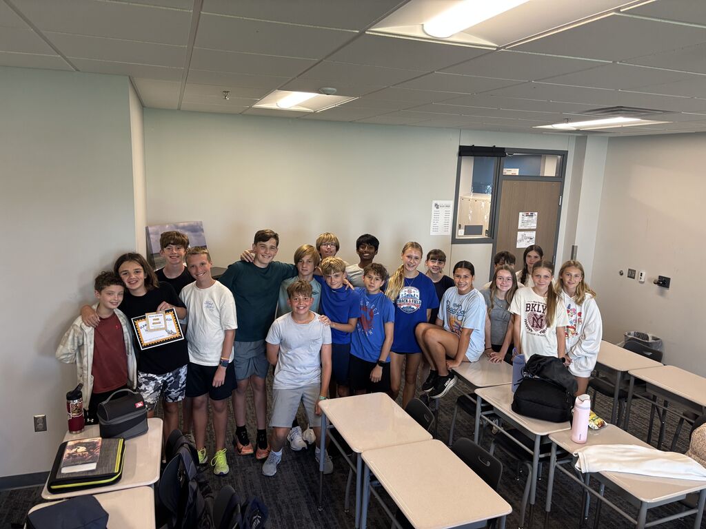 A group of students stand in a classroom smiling at the camera.