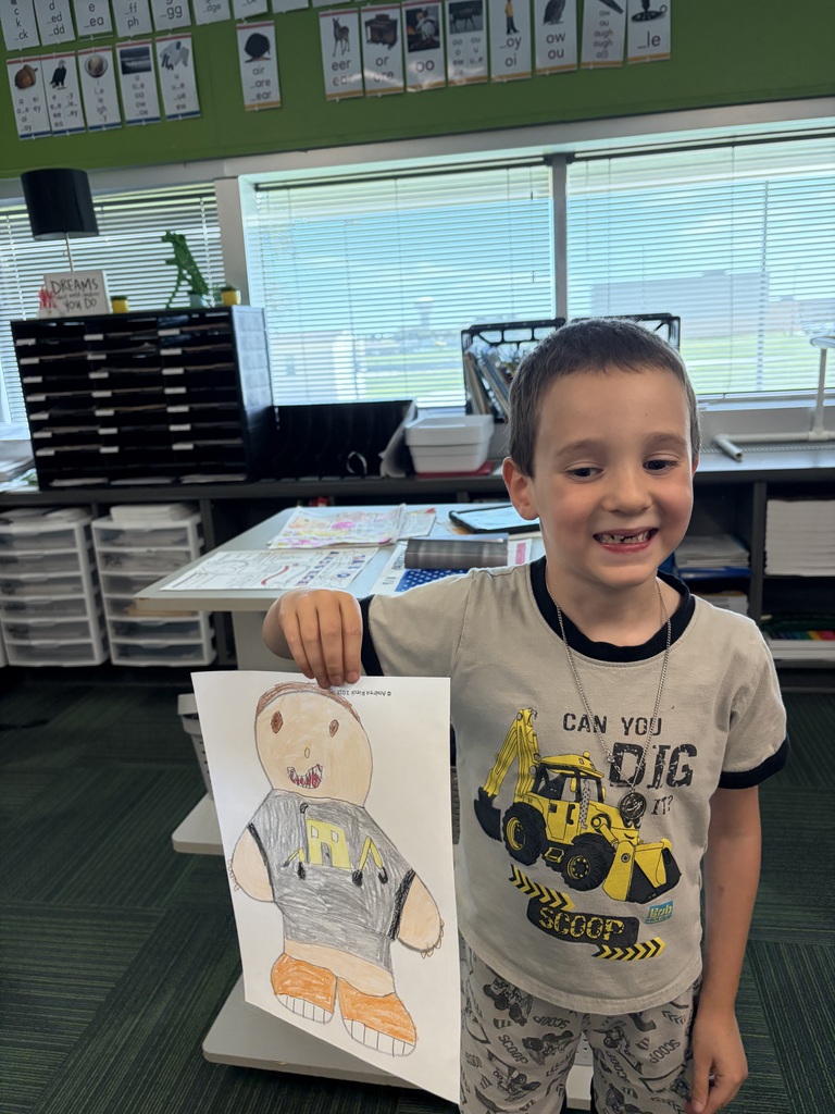 A young boy holding up his finished colored drawing of a person wearing a shirt that matches his own.