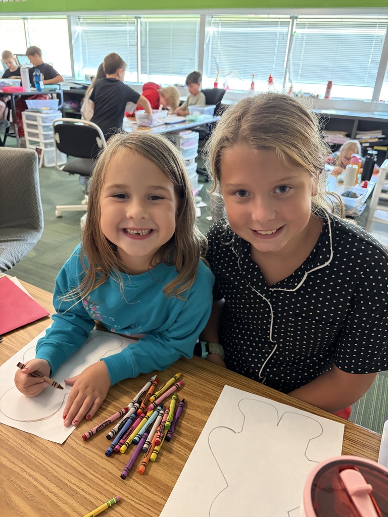 Two girls smiling together at their table while working with crayons on their gingerbread figure worksheets.