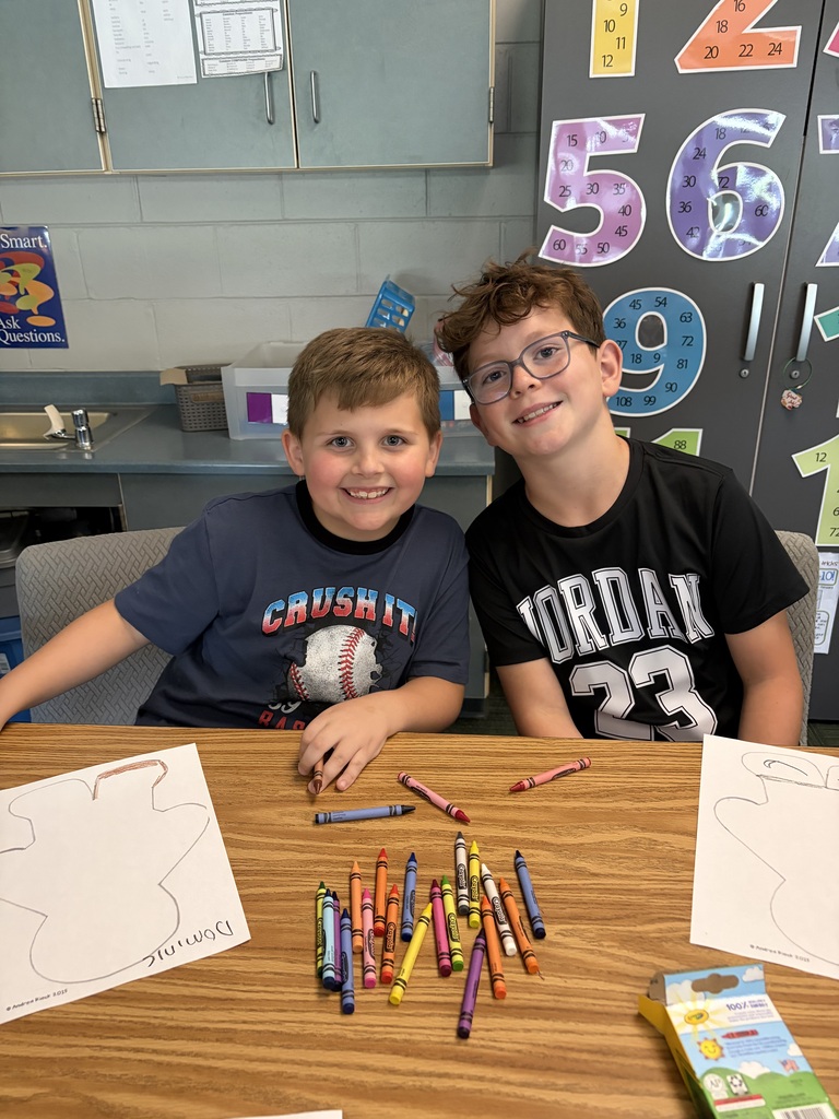 Two boys smiling at the camera with their crayon supply box and gingerbread coloring sheets laid out at their table.