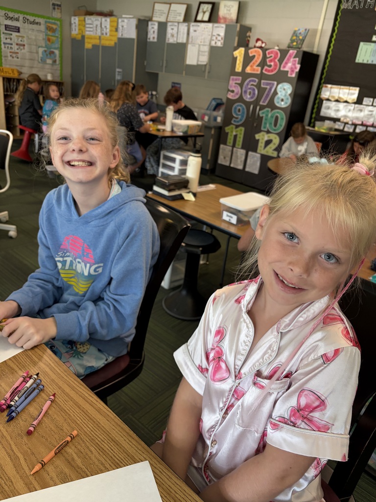 Two smiling girls sitting together at a wooden table with crayons, enjoying their joint coloring activity.