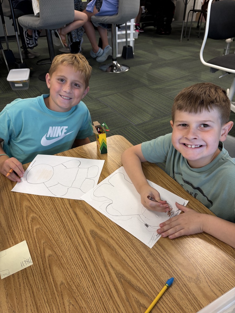 Two boys smiling at their desk while working together to color and design their gingerbread person cutouts.