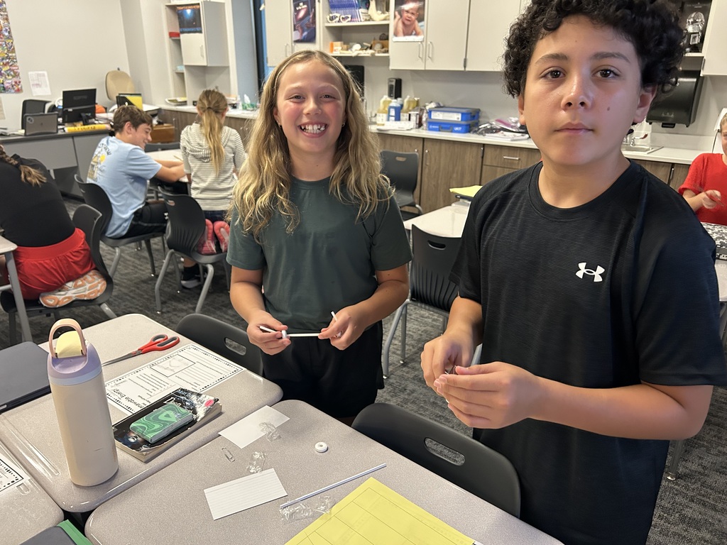 Students are smiling at the camera and working on building wind puft cars. 