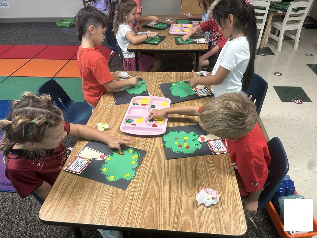 Four students are working on a fingerprint apple tree craft.