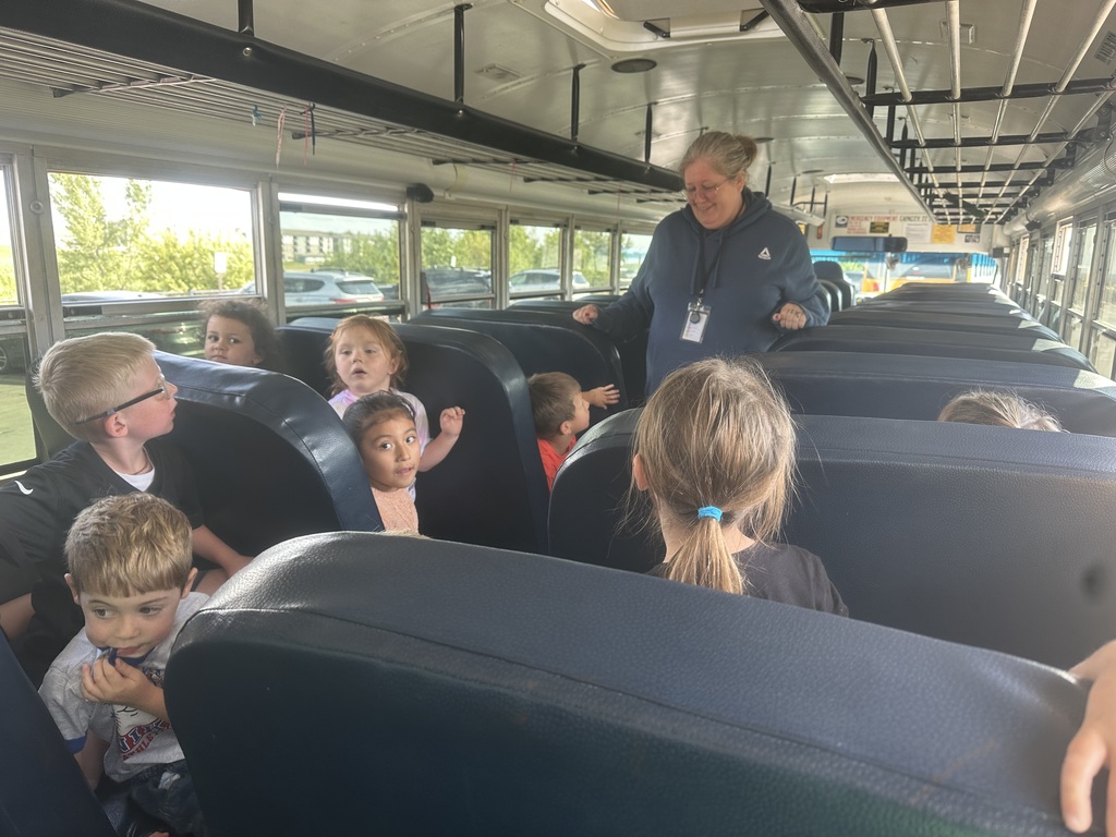 Students are sitting on a bus while the driver explains bus safety.