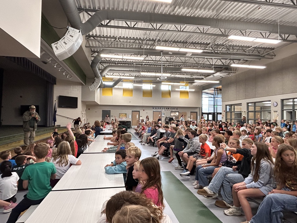 students sitting in the cafeteria listening to a speaker share about butterflies