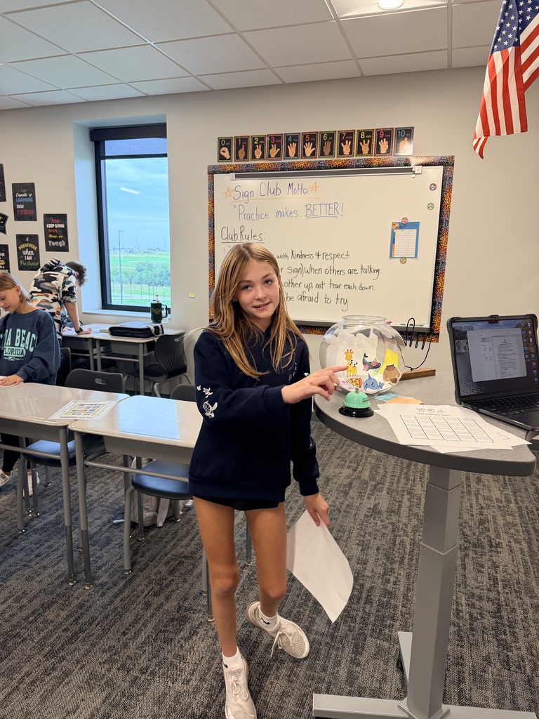 A student faces the camera and is getting ready to touch a bell on a desk. 