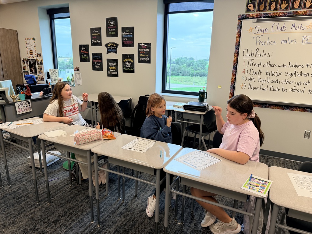 Two groups of students sit at desks and practice ASL. 