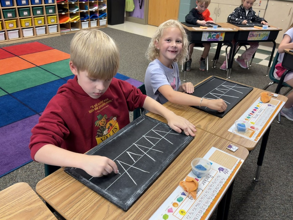 Students using chalkboards to practice their handwriting at desks. 