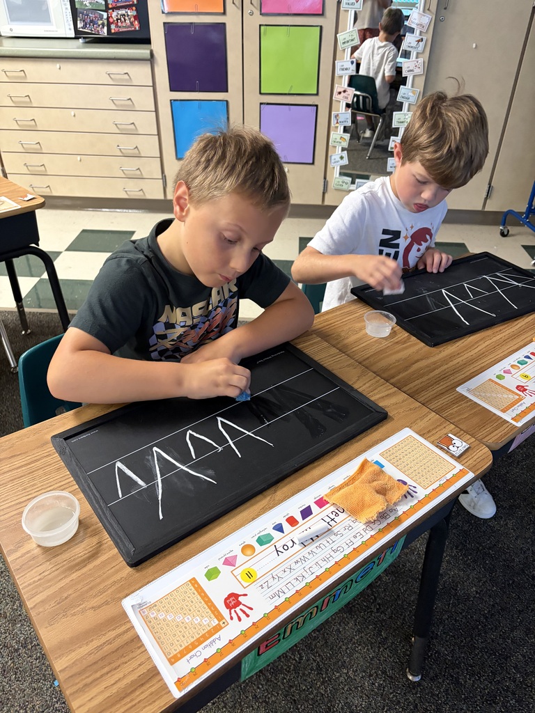 Students using chalkboards to practice their handwriting at desks. 