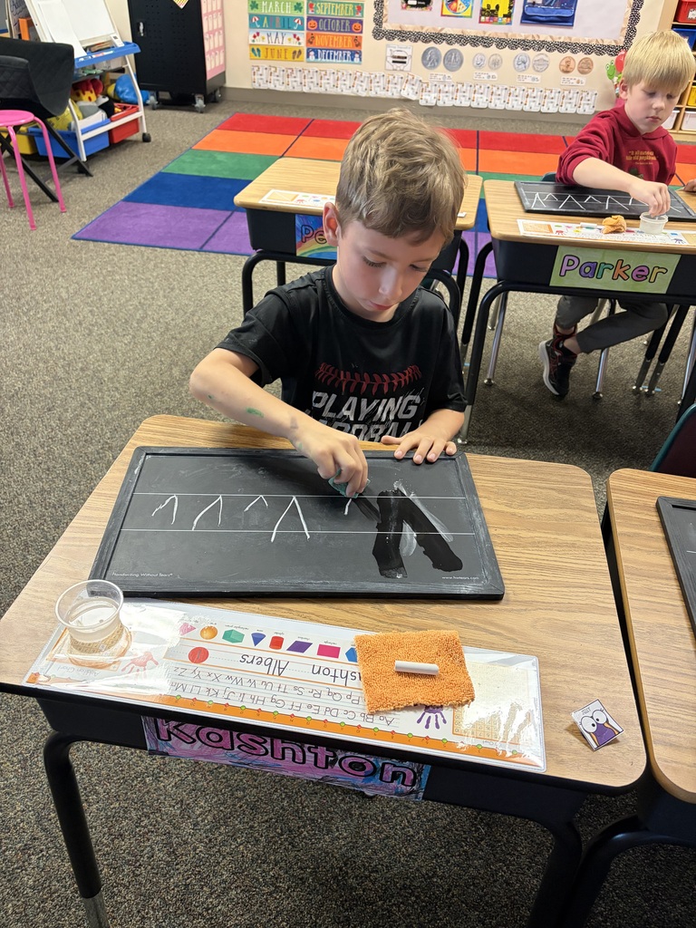 Students using chalkboards to practice their handwriting at desks. 