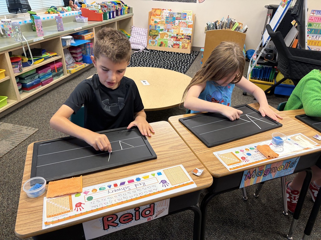 Students using chalkboards to practice their handwriting at desks. 
