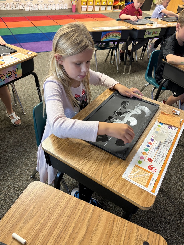 Students using chalkboards to practice their handwriting at desks. 