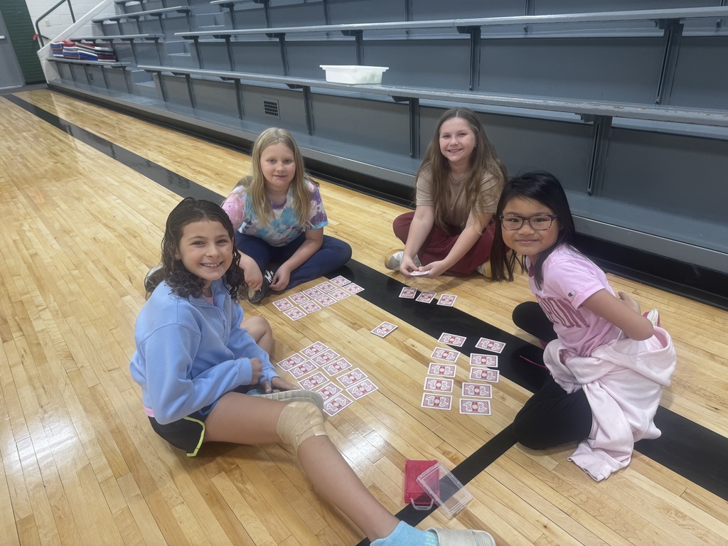 Four girls sitting in a circle on the gymnasium floor playing a card matching game.