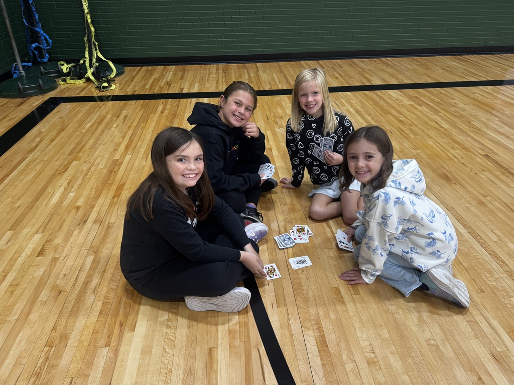 Four girls sitting cross-legged on the gym floor with playing cards spread between them.