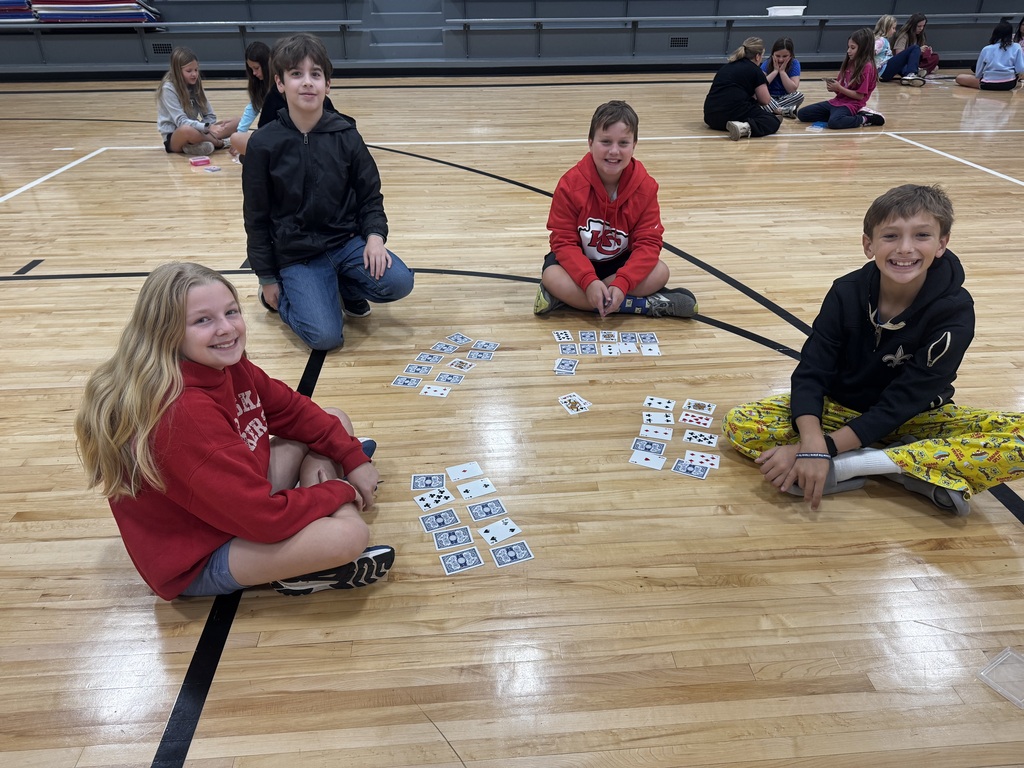 Four students sitting in a circle on the basketball court floor playing a card game together.