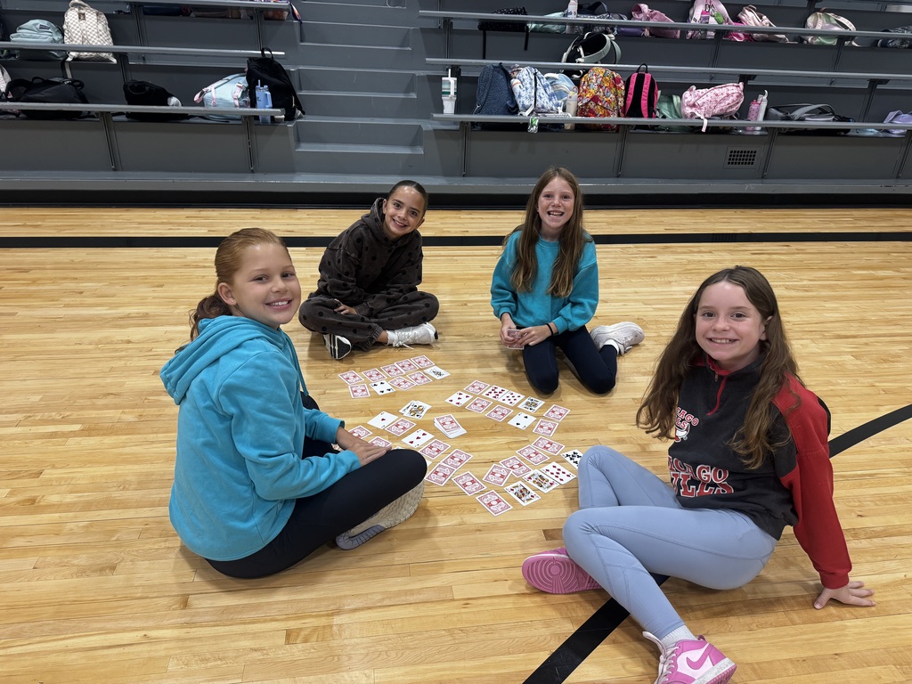Four girls sitting on the gymnasium court floor surrounded by organized playing card grids.