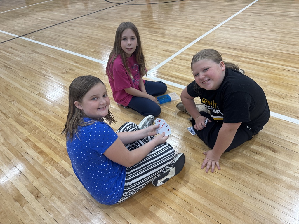 Three girls sitting in a circle on the court playing a card game together.