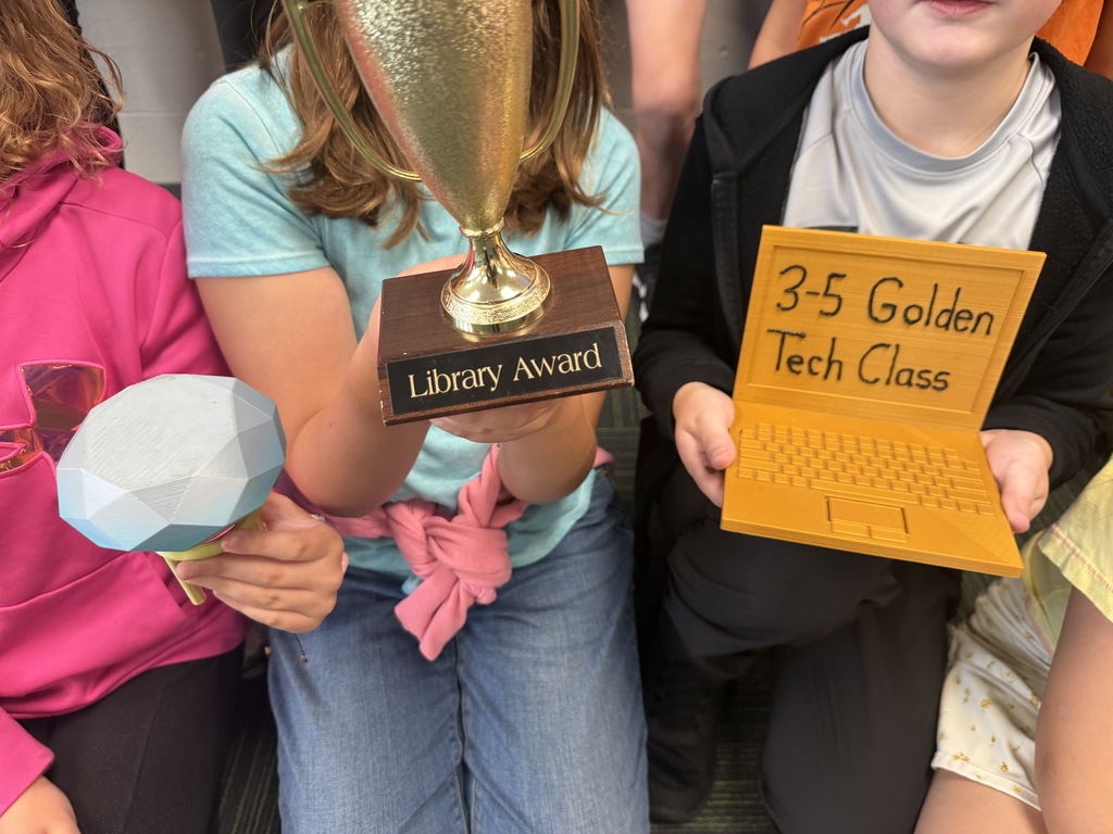 A close-up view of students holding up the Library Award trophy and the 3-5 Golden Tech Class award.