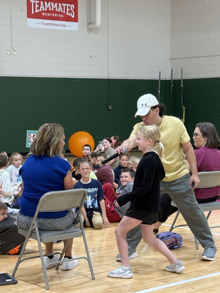 A speaker handing a microphone to a student standing in front of an audience in the gymnasium.