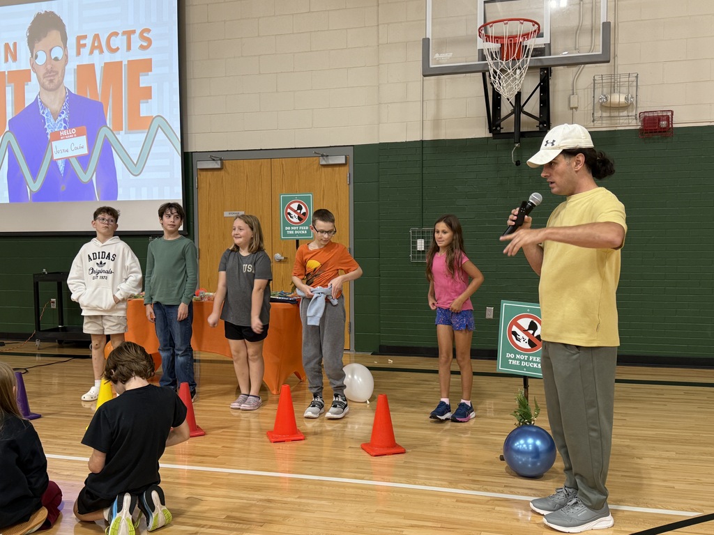 Students lined up on stage during an assembly while the presenter speaks to the audience.