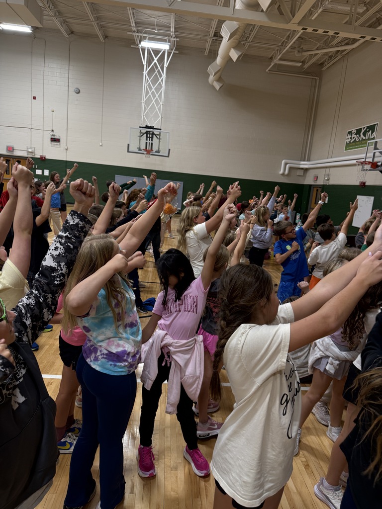 Students in the gymnasium raising their arms in the air together during a high-energy school activity.