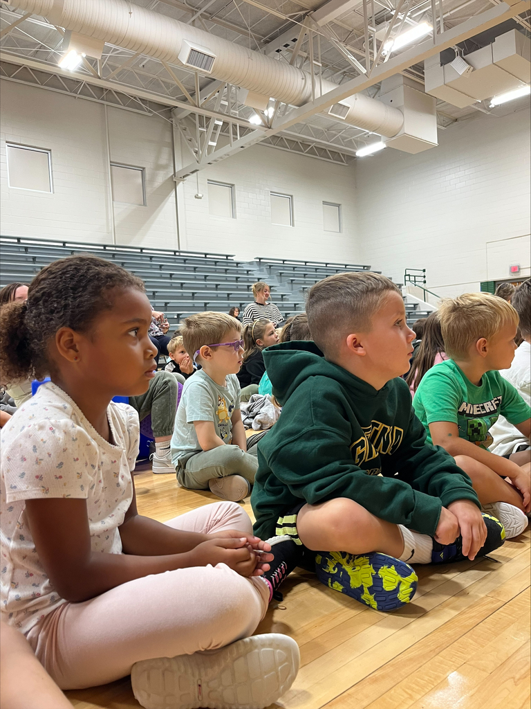 Students sitting on the gymnasium floor watching the presentation attentively.